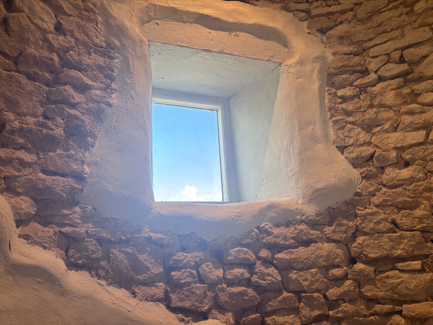 A small window opening to blue sky within old stone walls